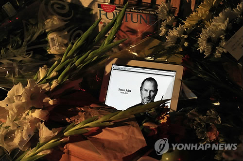 (AP=연합뉴스) 애플의 창업주 스티브 잡스가 숨진 5일(현지시간) 애플 본사 앞에 놓여진 조화 사이로 애플 제품 속 그의 사진이 보인다.